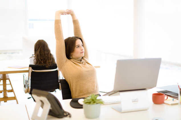 Chica haciendo estiramiento de brazos sentada en su oficina