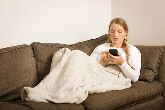 Chica acostada en un sofa cubierta con una manta