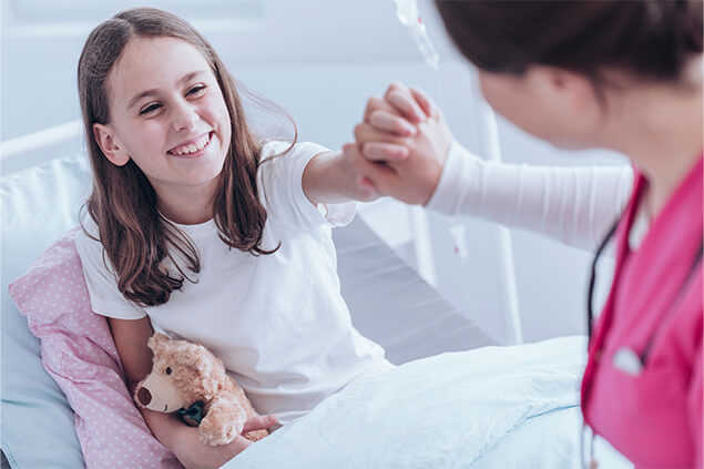 Niña en cama dandole la mano a enfermera