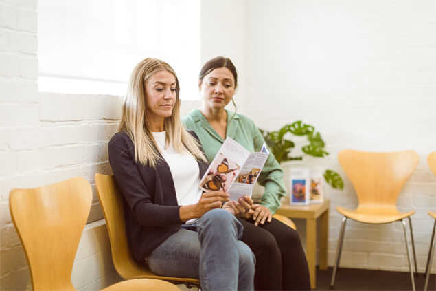 Dos mujeres sentadas mirando un tríptico
