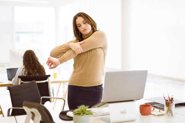 Chica realizando estiramiento de brazo frente al ordenador