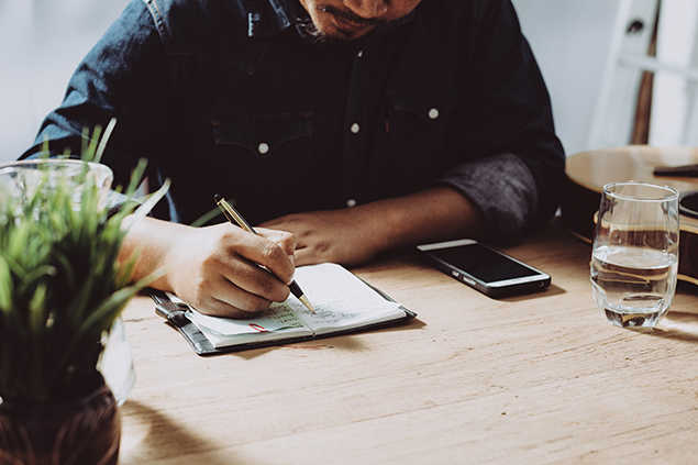 Hombre escribiendo en un bloc de notas sobre una mesa